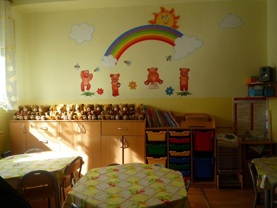 Sala z tęczą i misiami namalowanymi na ścianie, stolikami nakrytymi kolorowymi obrusami i półką pełną pluszowych misiów.
